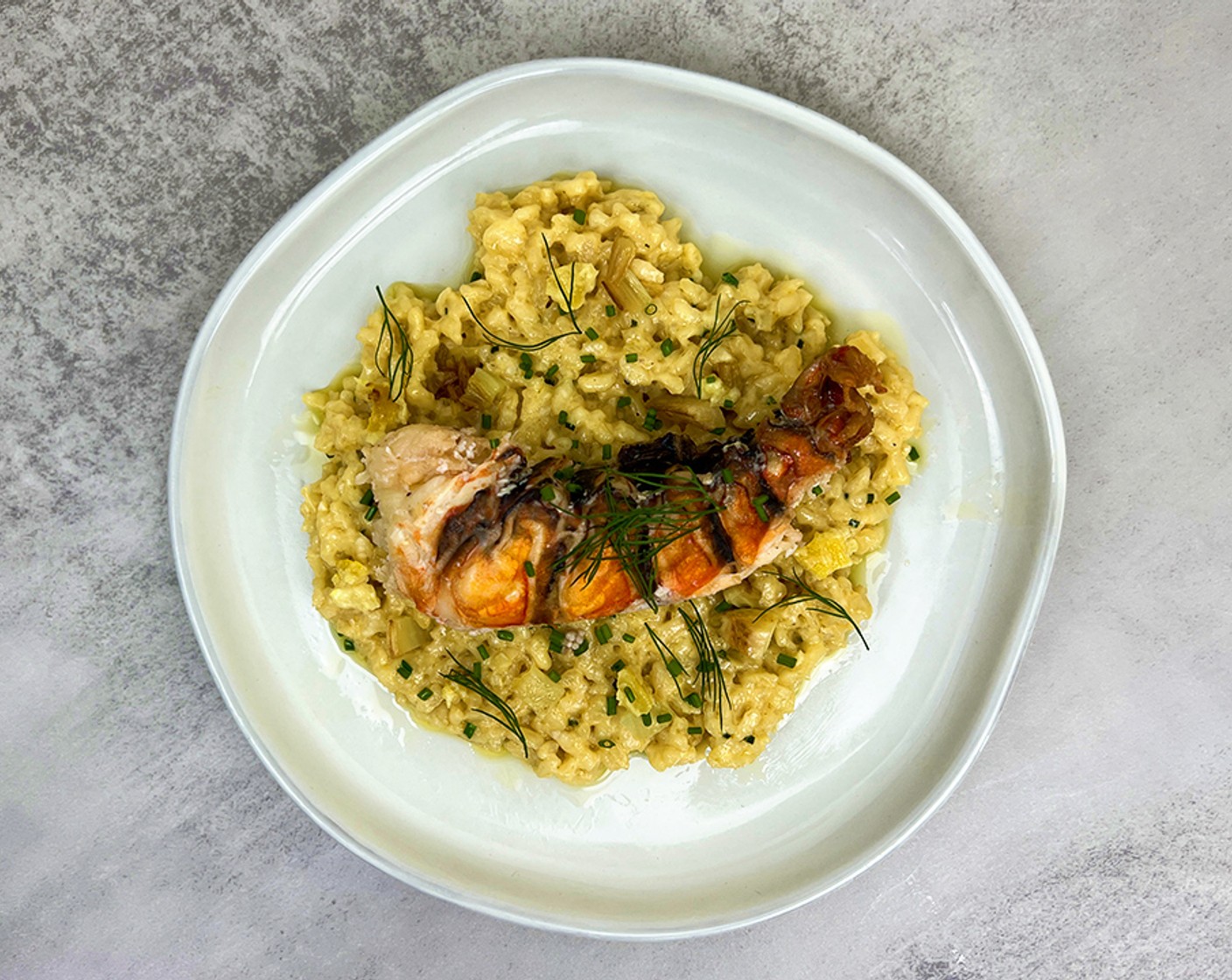 step 10 Plate: spoon the risotto into the center of a plate and top with more grated parmesan, Fresh Chives (2 Tbsp) and Fresh Parsley (2 Tbsp). Remove the skewer from the lobster tail, slice in half lengthwise, and place in the center of the risotto. Garnish with confit lemon and fennel fronds.