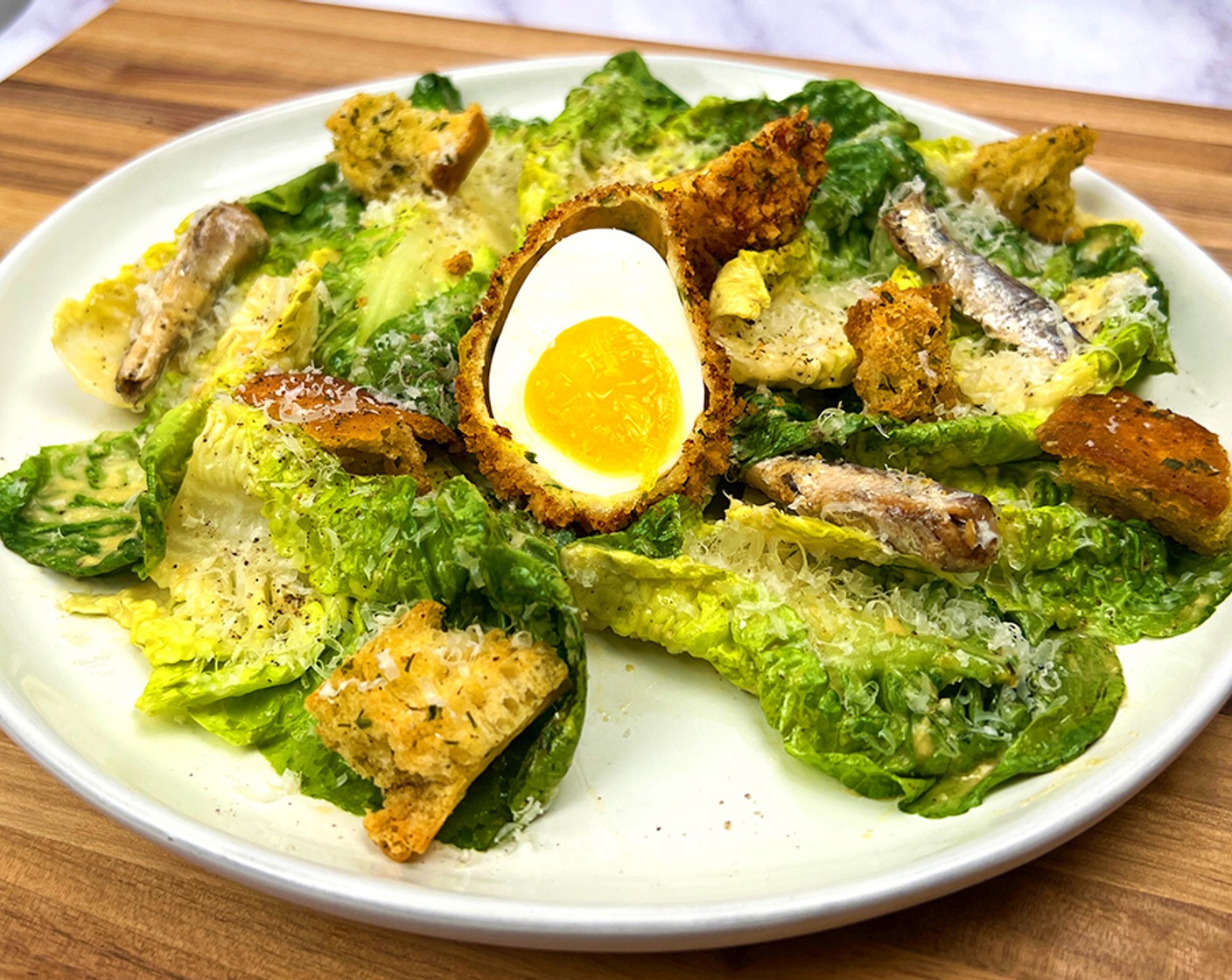 step 9 Assemble: In a large mixing bowl, toss the Little Gems Lettuce (1 bunch) with the caesar dressing until coated completely. Serve with the breaded egg, garlic croutons, Boquerones White Anchovies (as needed), Parmesan Cheese (as needed) and Freshly Ground Black Pepper (to taste).