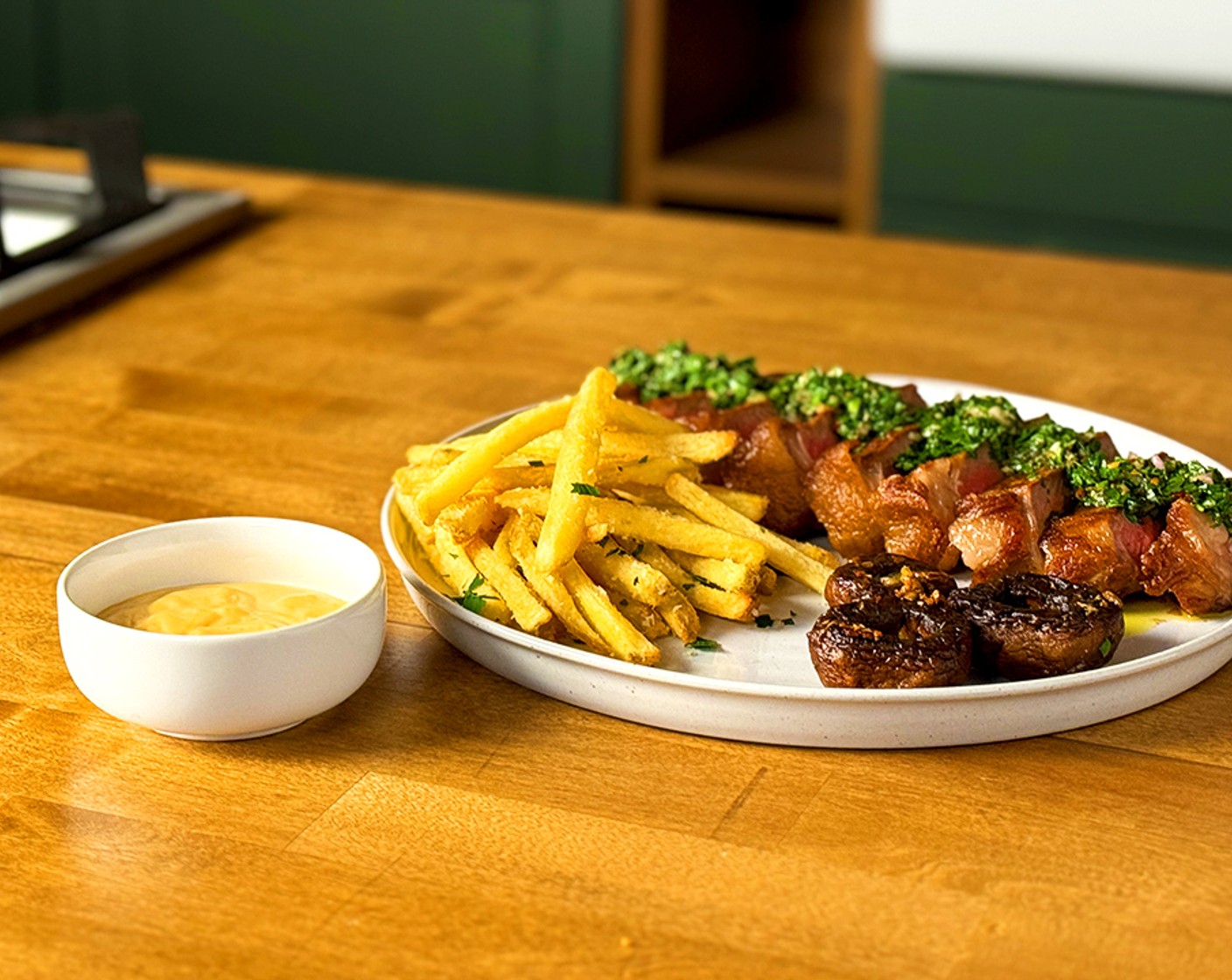 step 17 Plate: Arrange sliced NY Strip steaks on plates, top with chimichurri, a side of roasted garlic bulbs, sautéed baby bellas, spicy aioli, and truffle fries.